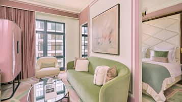 A room with a green sofa, a small table, a bed with a green bedspread, a pink armchair, and a large abstract painting on the wall.