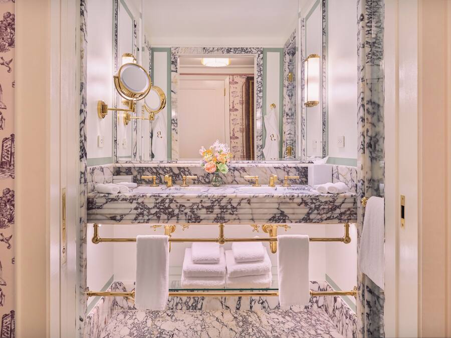 Une salle de bain avec un meuble-lavabo en marbre, des robinetteries dorées et un grand miroir.