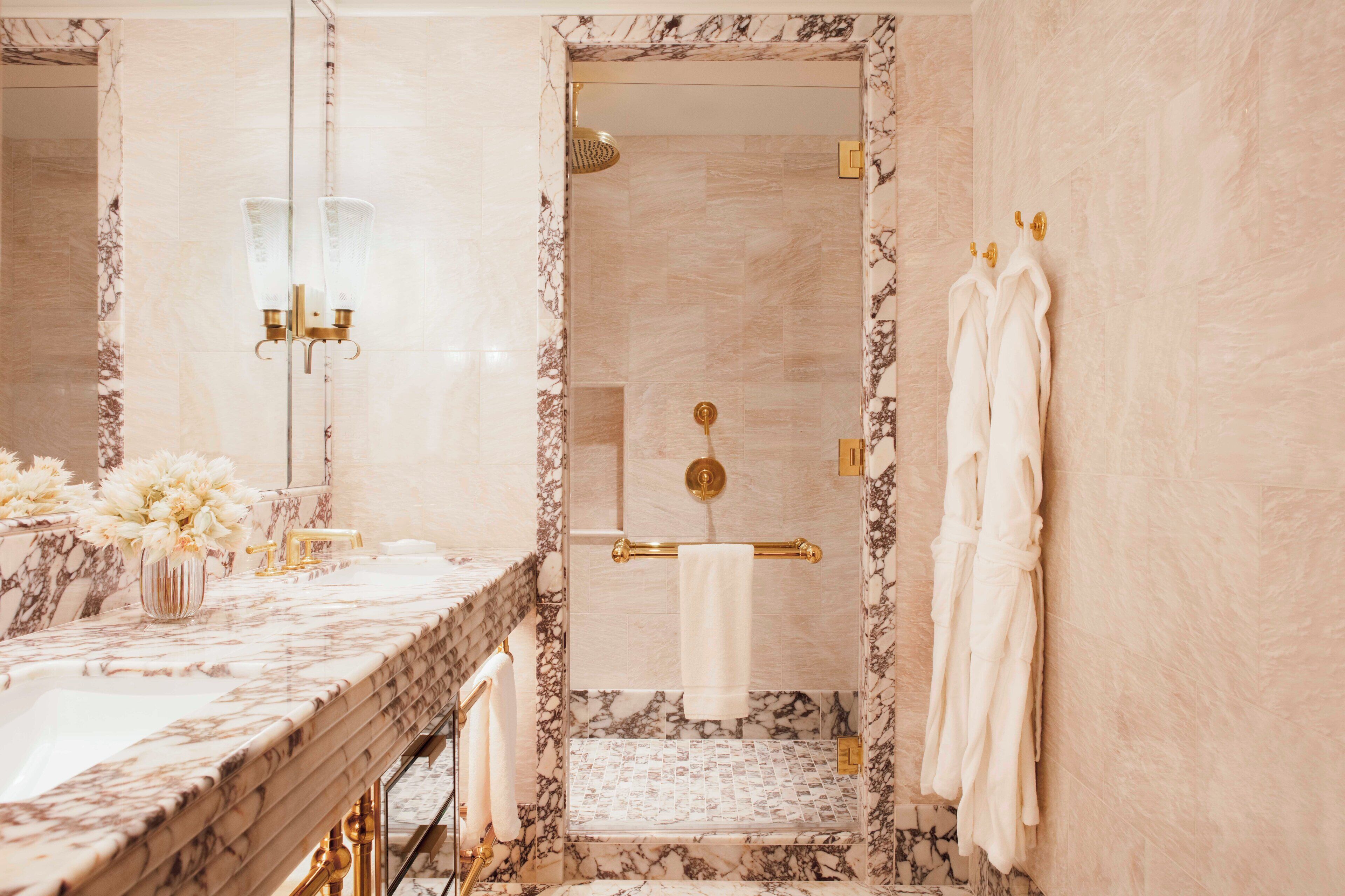 A bathroom with a marble vanity, a shower with a gold showerhead, and towels hanging on the wall.