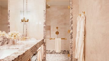 Un baño con tocador de mármol, ducha con ducha dorada y toallas colgadas en la pared.