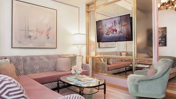A modern living room with a sofa, armchair, and coffee table. A television is mounted on the wall, and there is a large window with a view.