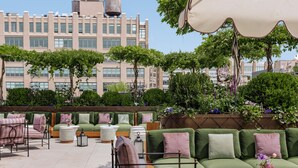 Terraza en la azotea con mobiliario exterior, incluyendo sofás y sillones, rodeada de plantas y vistas a la ciudad.