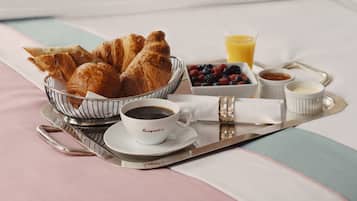 Bandeja de café da manhã com croissants, café, frutas vermelhas frescas e suco de laranja sobre a cama.