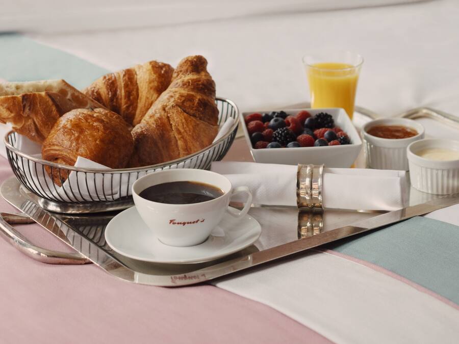Bandeja de café da manhã com croissants, café, frutas vermelhas frescas e suco de laranja sobre a cama.