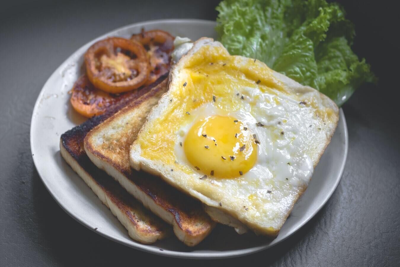 Een bord met een gebakken ei, geroosterd brood, gegrilde tomaten en een portie sla.