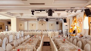 Une salle de banquet avec de longues tables dressées pour un événement formel, agrémentée de lustres, d’un éclairage de scène et d’une arche décorative faite de ballons.