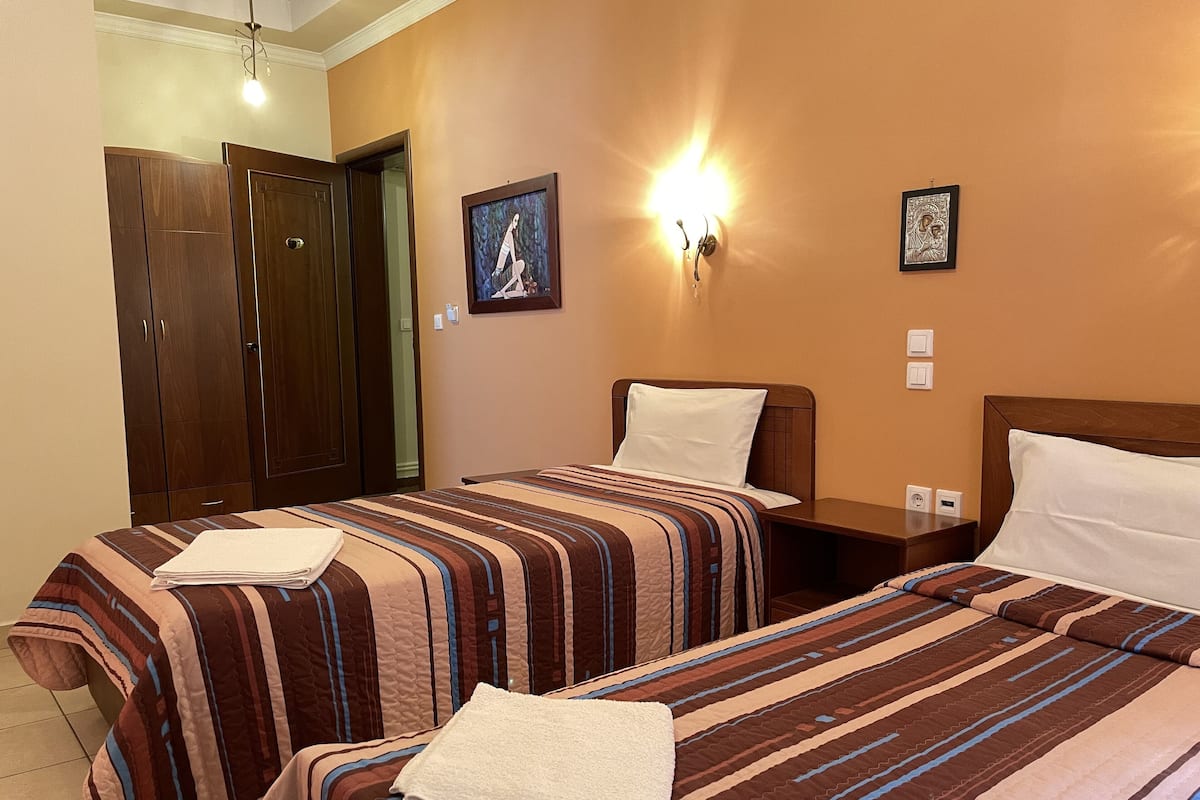 A hotel room with two beds, a wardrobe, a wall-mounted light, and a framed picture.