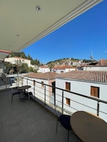 Un balcón con mesa y sillas, con vista a un pueblo de edificios con tejados de teja y una colina al fondo.