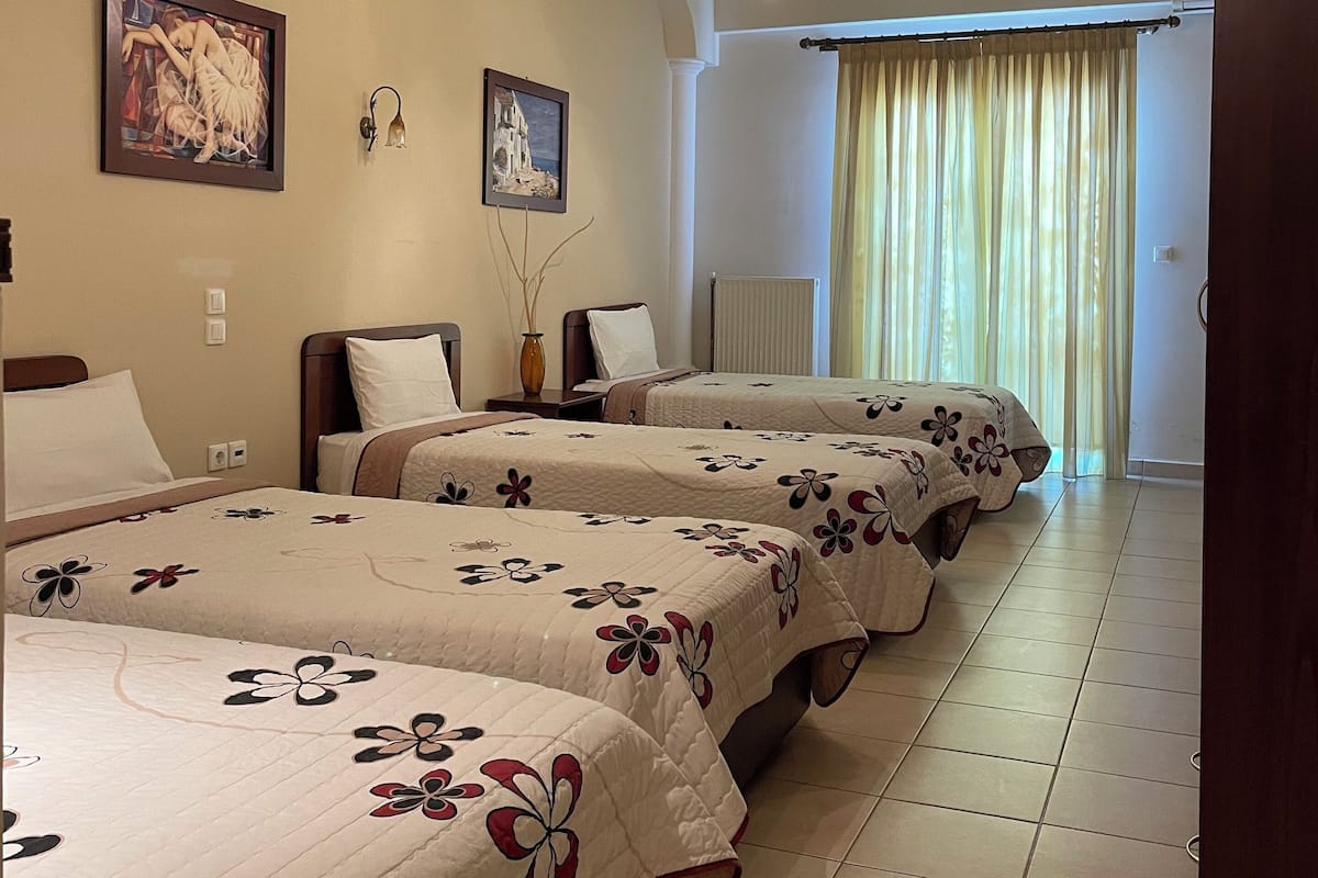 A hotel room with three beds, each with floral-patterned bedding, a chandelier, and two framed artworks on the wall.