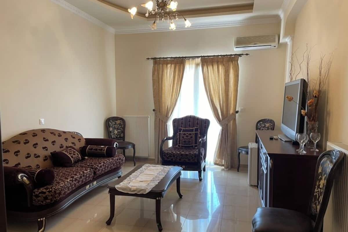 A living room with a sofa, armchair, coffee table, and a TV on a stand.