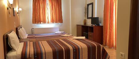 A hotel room with a large bed, a desk, a television, and a window with curtains.
