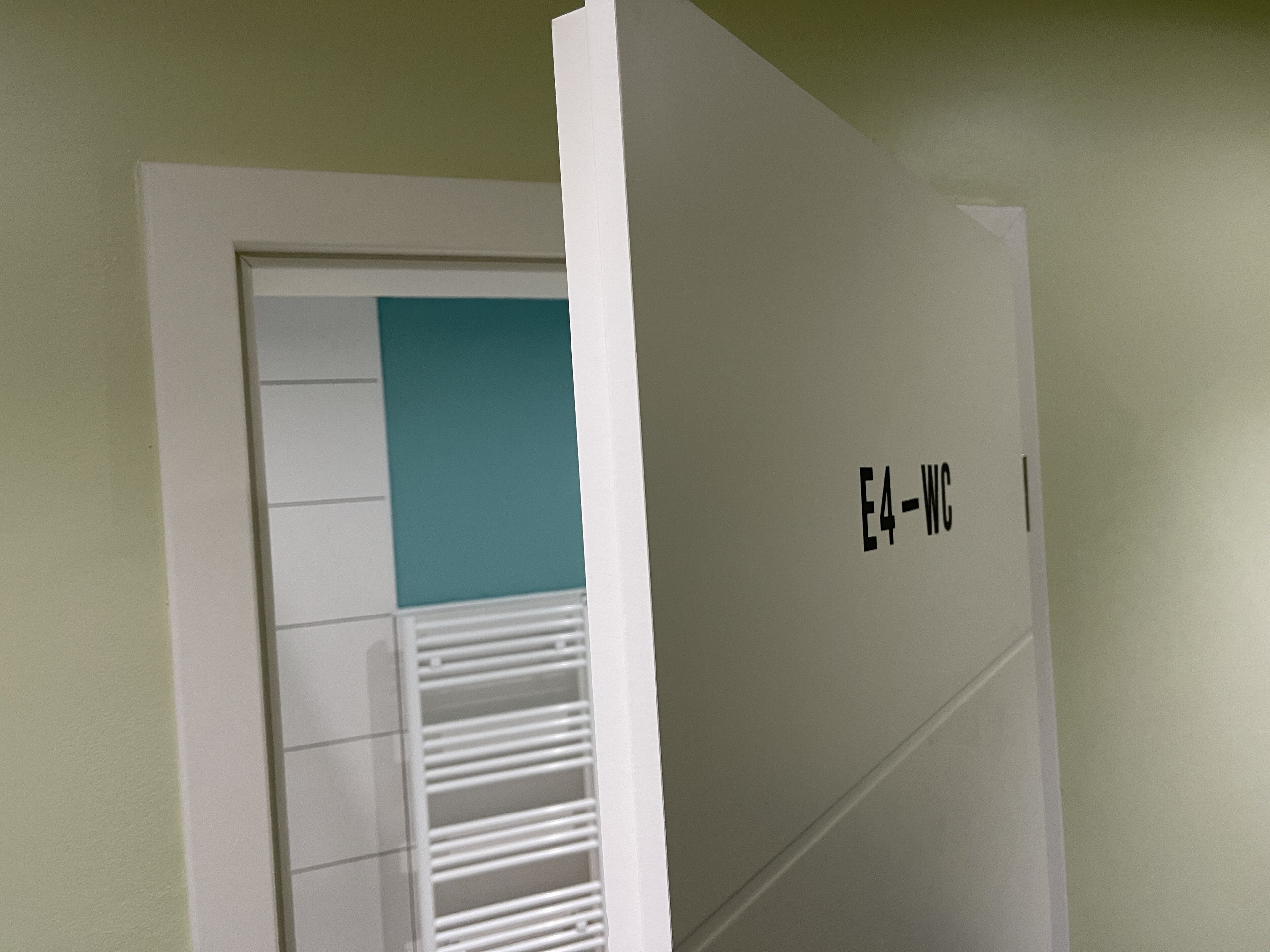 A room with a white door, a teal accent wall, and a white radiator.
