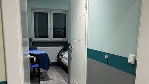 A narrow hallway with a bed, a chair, and a window. - Pension Waldau (Kassel)