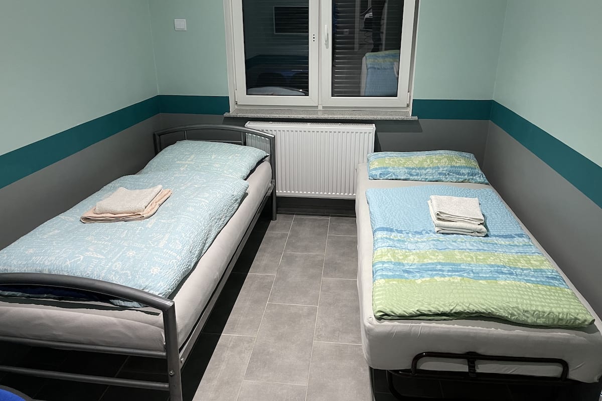 A small room with two single beds, a window, and a radiator.