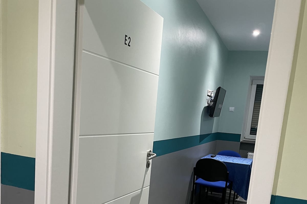A hallway with a door labeled "E2," a blue table with a blue tablecloth, and a chair.