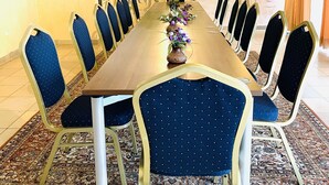 A dining room with a long table, blue upholstered chairs, and a decorative vase with flowers. - Pension Waldau (Kassel)