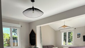 Un comedor con mesa y sillas de madera, una lámpara colgante negra y una pizarra con la palabra 'Welcome'.