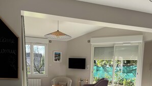 Una sala de estar moderna con comedor, una pizarra con escritura, televisor y vistas al exterior con vegetación.