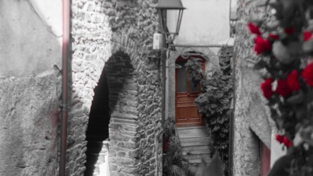 Un estrecho callejón con paredes de piedra, un farol y una puerta con un persiano rojo.