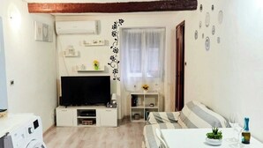 Un espacio habitable compacto con lavadora, televisor, mesa de comedor con sillas y sofá.