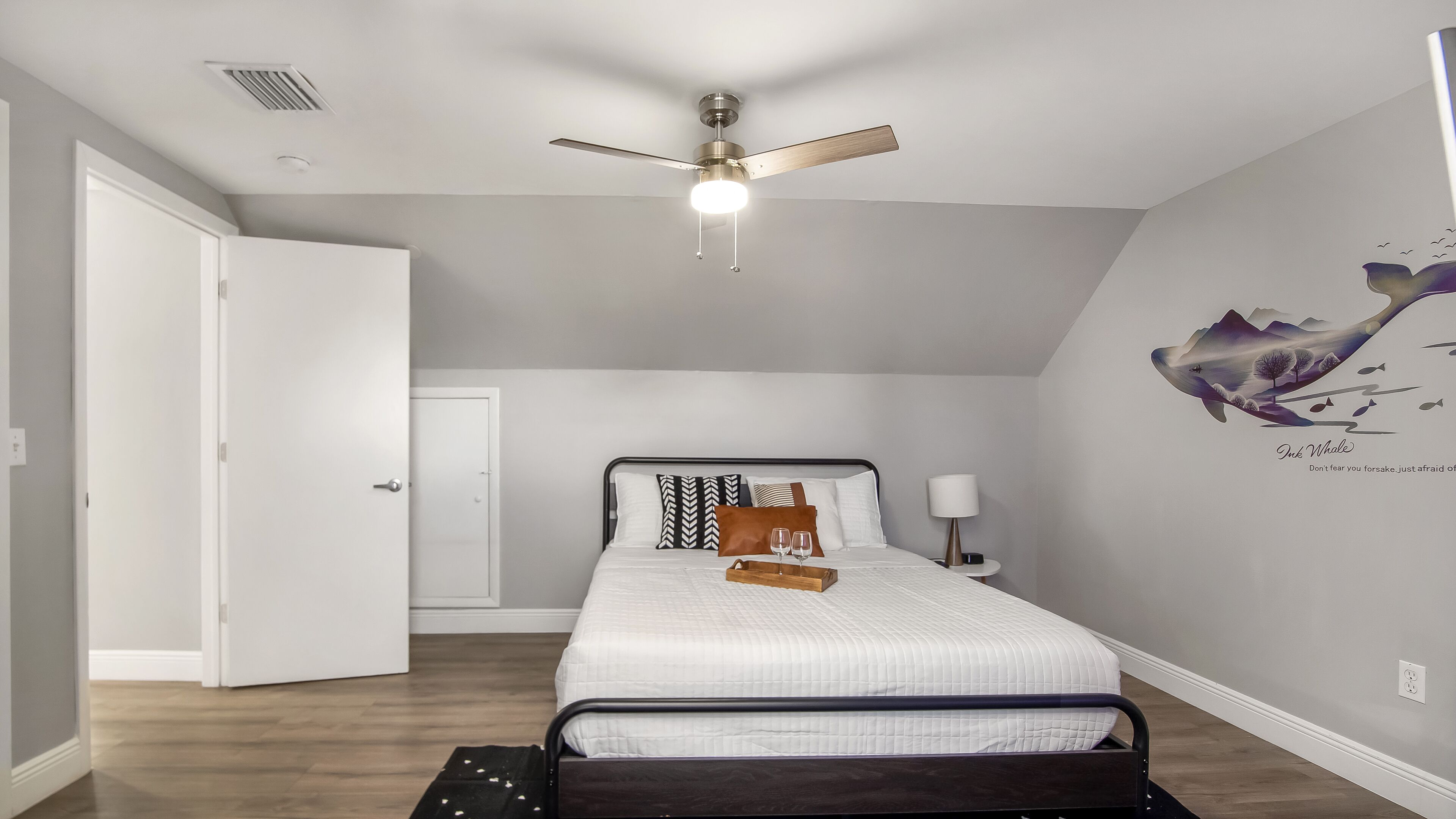 A bedroom with a bed, a ceiling fan, a nightstand, and a wall art piece.