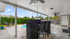 Eine überdachte Terrasse mit Pool, Sitzgelegenheiten im Freien und einem Deckenventilator.