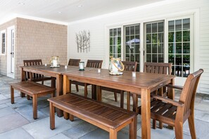 An outdoor patio with a wooden table and benches, large windows, and a brick wall. - 6 Bedroom 6.5 Baths Heated In-ground Pool Located in Dock Square! (Kennebunkport)