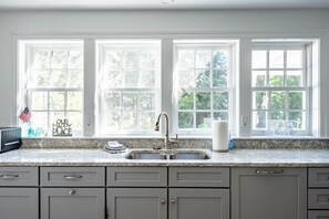 Enjoy a view of lush greenery from the large window in this kitchen, featuring a granite countertop, stainless steel sink, and range hood.