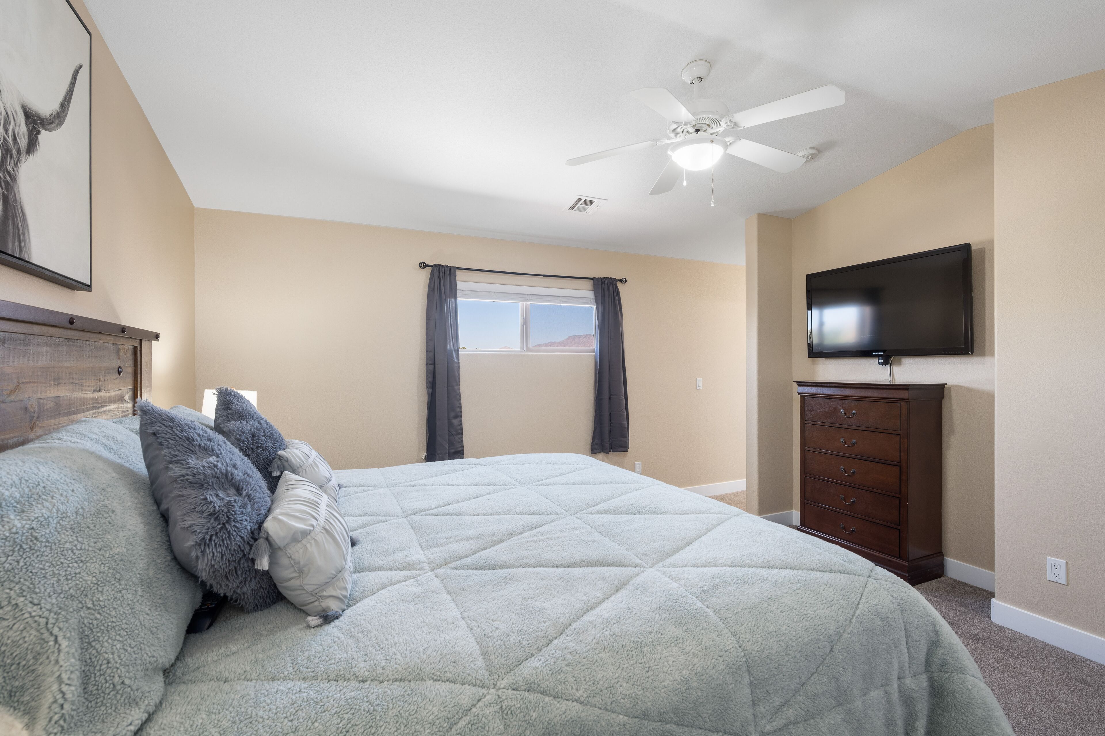Ein Schlafzimmer mit Bett, Deckenventilator, Kommode und Fernseher.