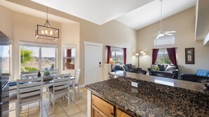 A spacious kitchen with granite countertops, a dining area with white chairs, and a living room with a sofa and a ceiling fan. - The Oasis - Golf - Pool - Hot Tub - Condo with a View. (Mesquite)