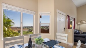 A dining area with a table set for two, a bottle of wine, a potted plant, and a view of the landscape through large windows. - The Oasis - Golf - Pool - Hot Tub - Condo with a View. (Mesquite)