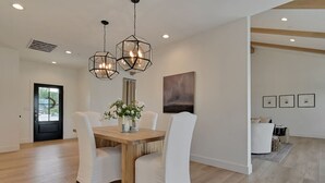 Un comedor con mesa de madera, sillas blancas y una lámpara colgante moderna.