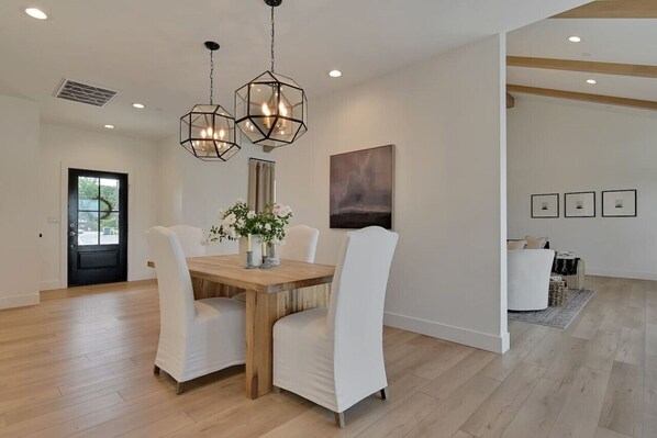 A dining area with a wooden table, white chairs, and a modern pendant light fixture.