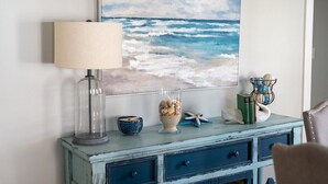 A room with a wall-mounted painting of a beach scene, a lamp, a decorative vase with seashells, and a blue dresser with drawers. - Beautiful Beach Cottage in Downtown Bristol (Bristol)