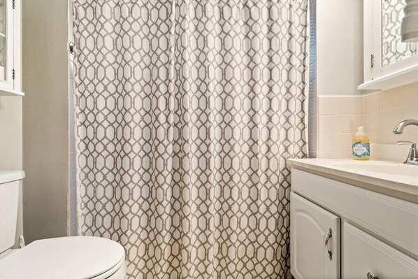 A bathroom with a patterned shower curtain, a toilet, and a sink with a soap dispenser. - Beautiful Beach Cottage in Downtown Bristol (Bristol)