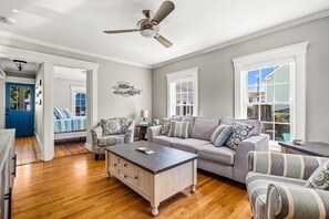 A spacious living room with hardwood floors, a gray sofa, patterned armchairs, a coffee table, and a ceiling fan. - Beautiful Beach Cottage in Downtown Bristol (Bristol)