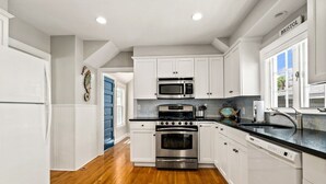 A modern kitchen with white cabinets, stainless steel appliances, and a wooden floor. - Beautiful Beach Cottage in Downtown Bristol (Bristol)