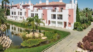 A multi-story hotel with balconies, a swimming pool, and a landscaped garden with a pond. - Modern Apartment with Free Wifi and communal swimming pool in O POMAR Cabanas (Cabanas de Tavira)
