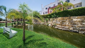 A landscaped garden with a pond, stone wall, and a white bench. - Modern Apartment with Free Wifi and communal swimming pool in O POMAR Cabanas (Cabanas de Tavira)