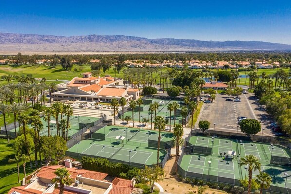 A large sports complex with multiple tennis courts, surrounded by residential buildings and palm trees.