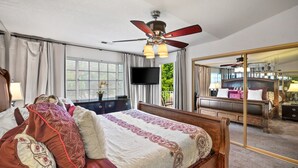 Un dormitorio con cama, ventilador de techo, televisión, cómoda y un espejo grande.