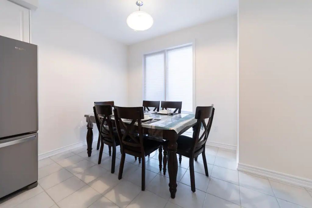 A dining area with a table and chairs, a refrigerator, and a window with blinds.