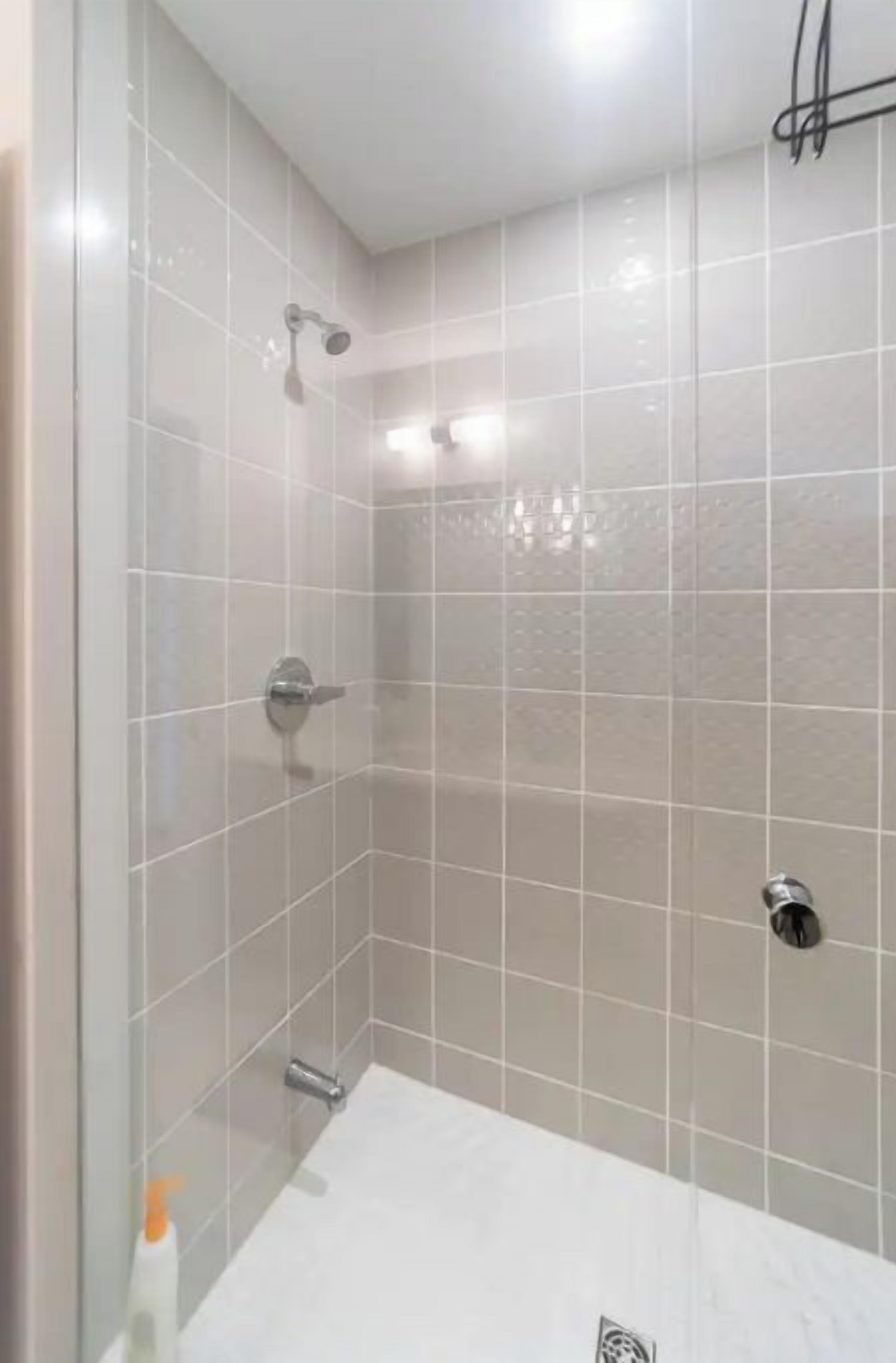 Casa de banho moderna com cabine de duche em vidro, lavatório branco e chuveiro manual.