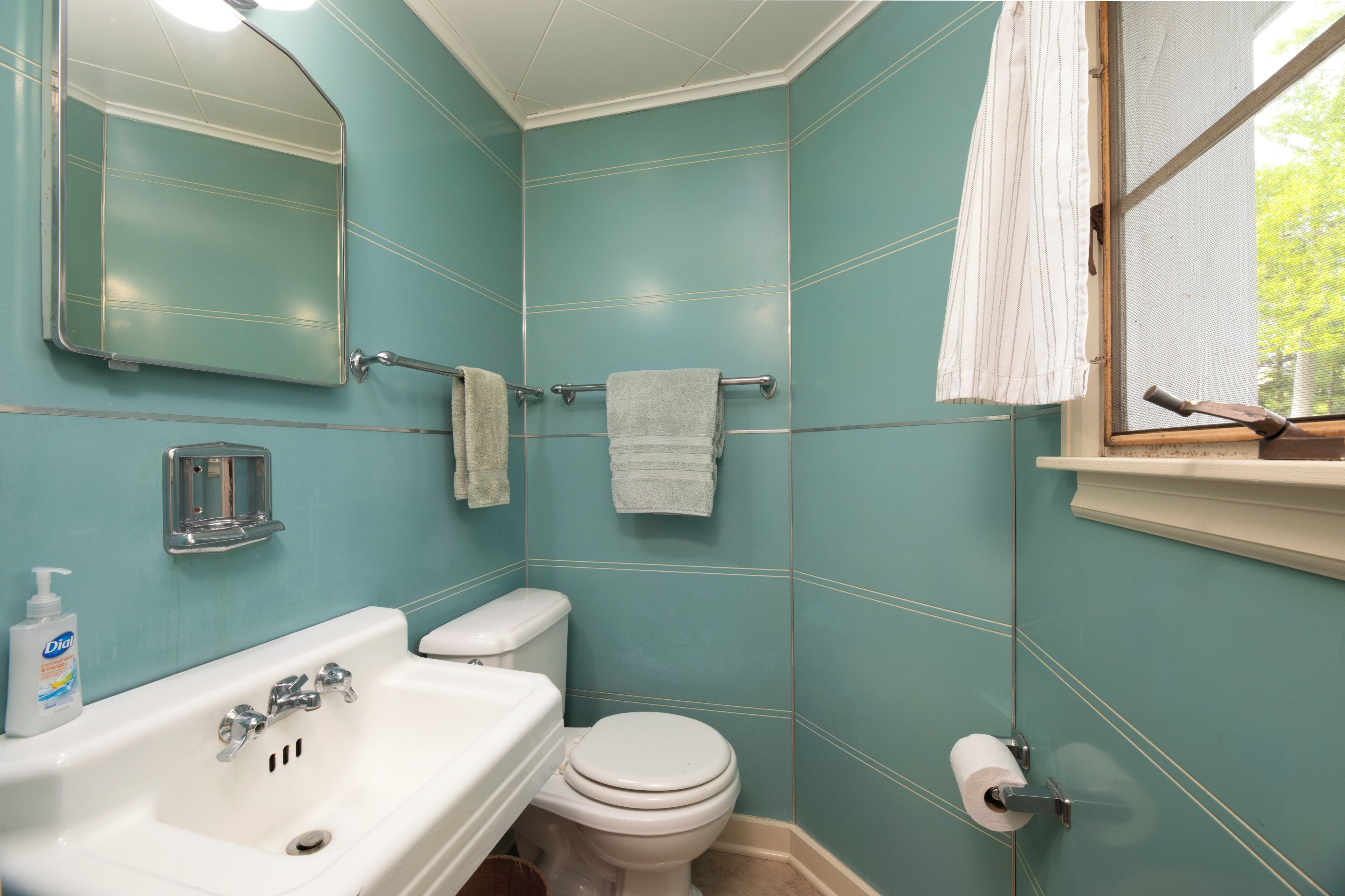 Een badkamer met een wastafel, toilet, spiegel en raam.