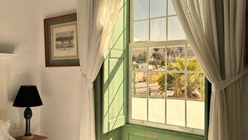 Una habitación con una cama, una mesita de noche con lámpara, un cuadro en la pared y una ventana con cortinas.