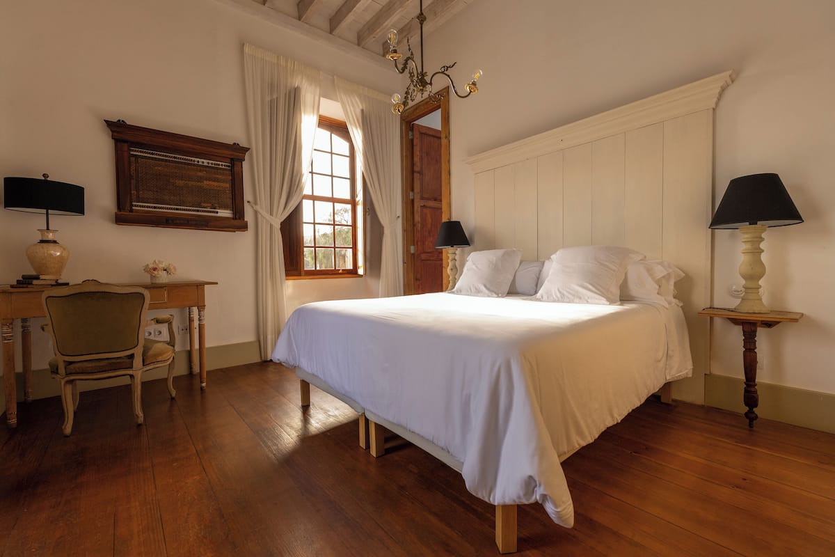 Ein Schlafzimmer mit einem hölzernen Bett, einem Schreibtisch mit Stuhl, einer Lampe und einem Fenster mit Vorhängen.