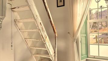 Una escalera rústica con detalles de madera, un sillón con tapicería floral y una ventana que ofrece vistas de cactus.