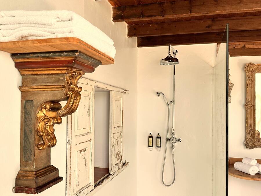Un baño con techo de madera, un lavabo con base decorativa, una ducha con cabezal de mano y un espejo con marco de madera.