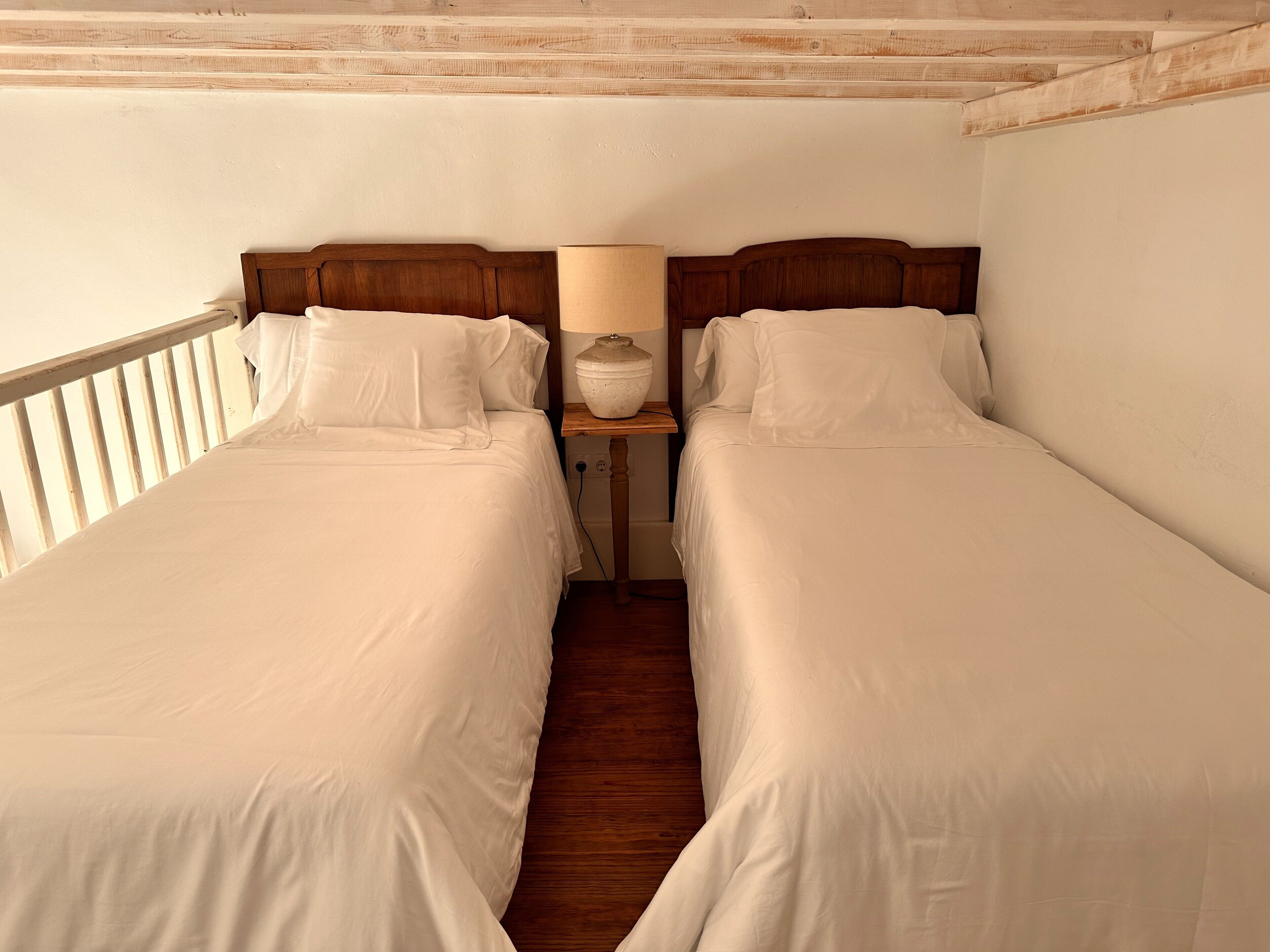 Una habitación con dos camas individuales, cabeceros de madera, ropa de cama blanca y una mesita de noche con lámpara.