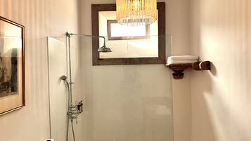 Un baño con ducha de vidrio, una lámpara colgante, un cuadro en la pared y un perchero para toallas.